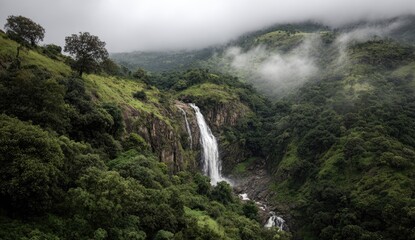 Lush green valley with waterfall cascading down rocky cliff. Misty mountains in the background