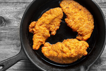 Southern fried chicken cooked in a cast iron frying pan with cooking oil. On a wooden board background..