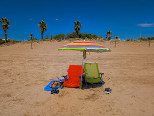 Parasol con dos sillas en una playa desierta con palmeras