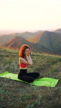 A woman practices yoga on a mat atop a mountain