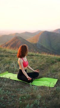 A woman practices yoga on a mat atop a mountain