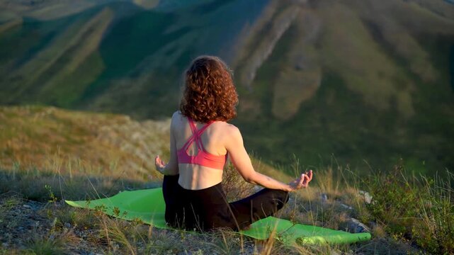 A woman practices yoga in a lotus position on a hilltop at sunset