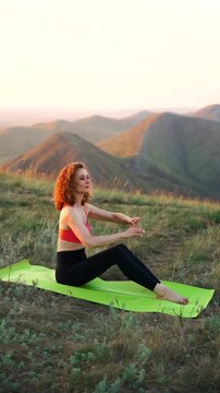 A woman practices yoga on a mat atop a mountain