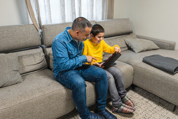 Father and son enjoying quality time together, exploring a digital tablet on a comfortable sofa in their living room, creating a warm and connected family atmosphere