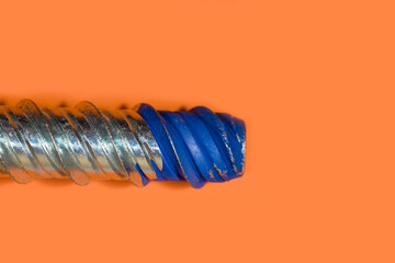 Large machined screw thread with blue lock paint on orange background close up view.