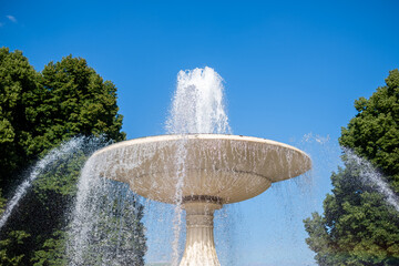 Warsaw, Poland, Saxon Garden, Majestic fountain with cascading water surrounded by lush green trees under a blue sky, creating a serene and refreshing outdoor atmosphere for relaxation and enjoyment