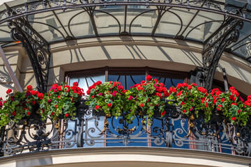 Elegant balcony adorned with vibrant red flowers, showcasing intricate wrought iron details,...