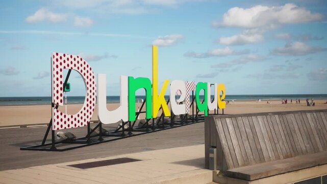 Colorful Dunkerque beach sign with sandy coast and sea in the background.