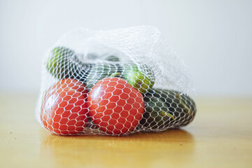 Fresh vegetables in reusable mesh produce bag on kitchen table. Zero waste lifestyle, plastic-free grocery shopping concept. Eco-friendly packaging alternatives for environmentally conscious consumers
