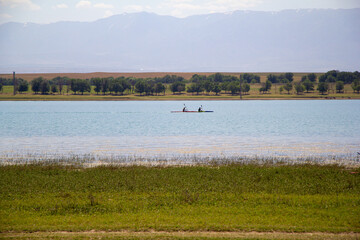 Two people kayaking on a calm lake with mountains in the background