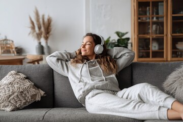 Fototapeta premium young woman with headphones lounging on a sofa at home portrait of a girl relaxing in a modern living room interior