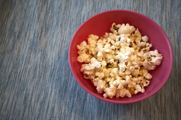 Close-up of fresh popcorn served in a pastel pink bowl against a solid blue background with copy space.