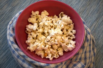Close-up of popcorn in a pastel pink bowl placed on a blue checkered kitchen towel. Minimal composition with copy space.