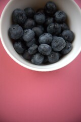 Fresh blueberries in a simple white bowl isolated on a pastel pink background. Close-up food concept with copy space.