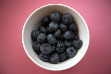 Fresh blueberries in a simple white bowl isolated on a pastel pink background. Close-up food concept with copy space.