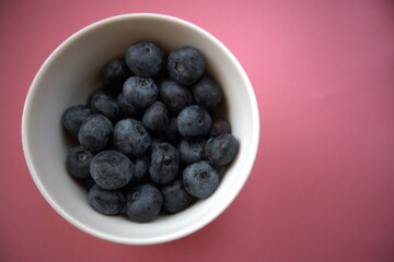 Fresh blueberries in a simple white bowl isolated on a pastel pink background. Close-up food concept with copy space.