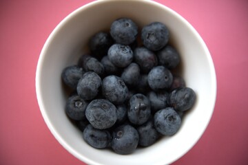 Fresh blueberries in a simple white bowl isolated on a pastel pink background. Close-up food concept with copy space.