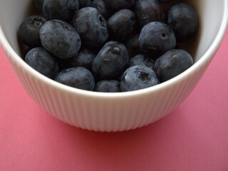 Fresh blueberries in a simple white bowl isolated on a pastel pink background. Close-up food concept with copy space.