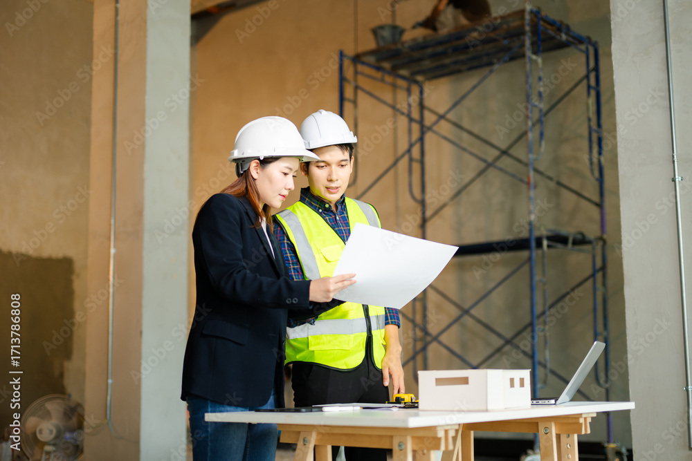 Poster construction engineer in a safety vest and an architect with a hard hat examine blueprints and a sca
