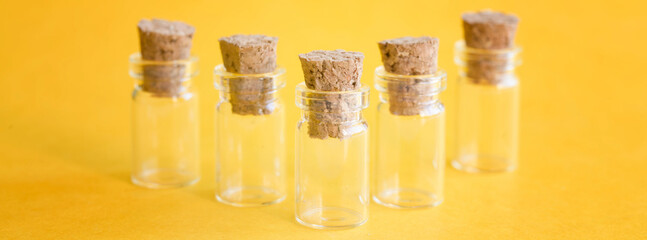 Five tiny clear glass vials with natural cork stoppers on vivid yellow; selective‑focus lab still life, wide banner for science, research and sampling themes. Photo