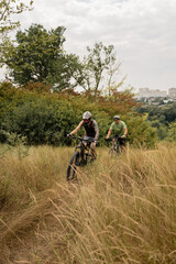 Cyclists enjoy a grassy nature path surrounded by trees and plants during daytime.