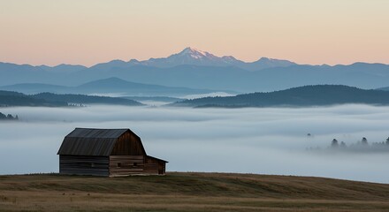 Rustic wooden barn nestled on a grassy hill overlooking misty valleys and distant snow-capped mountains at dawn.