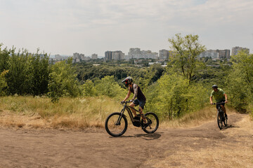 Cyclists riding bicycles on a dirt trail near a city on a sunny day.