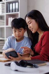 Obraz premium Asian mother helping son with homework and using calculator
