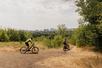 Cyclists enjoying a scenic path near an urban area with trees and sunshine.