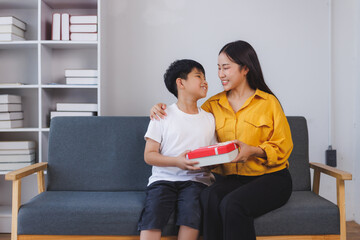 Asian mother and son exchanging gifts on a sofa at home