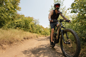 Cyclist riding a mountain bike on a natural dirt path surrounded by lush greenery.