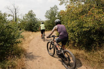 Two people enjoying outdoor cycling along a forest path on a sunny day