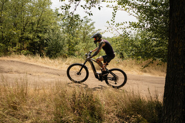 Person riding an electric mountain bike through a forest trail under a sunny sky