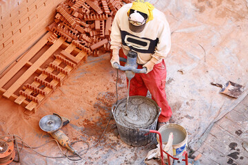 Perspectiva aérea cenital de obrero mezclando cemento y taladrando con martillo hidráulico en la obra entre ladrillos, hormigón, radial, material y otras herramientas