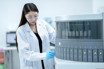 A medical technician in a hospital lab operates a large automated testing machine. She is loading...