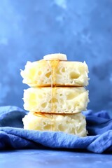 Stack of fluffy pancakes drizzled with honey, with a pat of butter on top, set against a blue background.