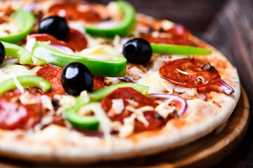 Pizza with chorizo ​​sausage, mozzarella cheese, green pepper and black olives. Rustic wooden background. Soft focus.	