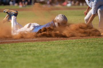 Tension peaks in this high-stakes baseball moment: the runner slides head-first into third base as a dust storm rises and the third baseman reaches to tag him out.