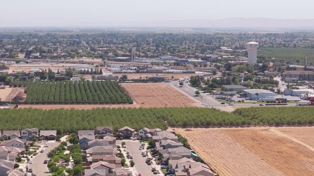 Elevated aerial shot showing residential area, farmland, busy road, water tower, and commercial zone in Ripon California.