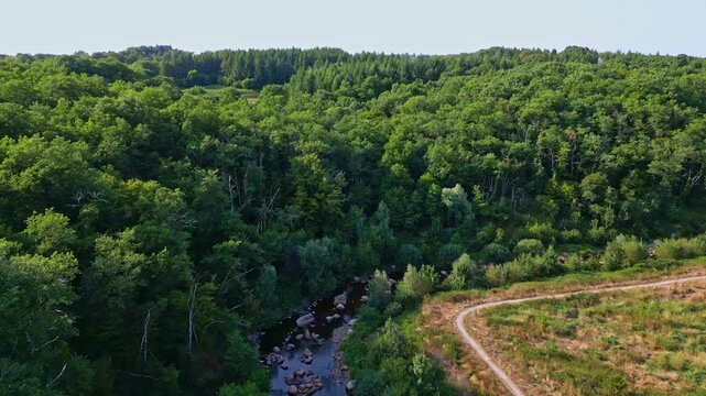 Drone fly at a lush green Gu&eacute; giraud forest with rocky visible stream and dirt track, Saint-Junien, Haute-Vienne, France.