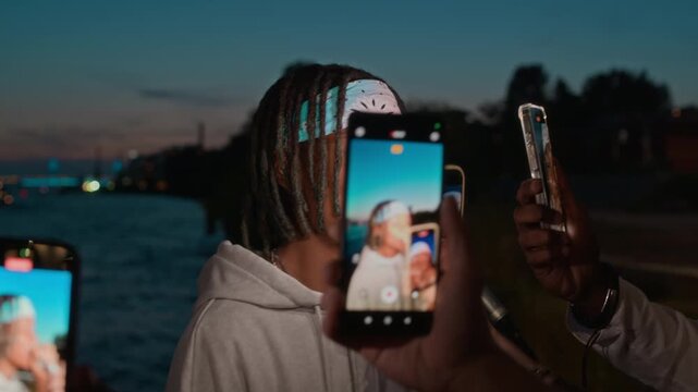 Group of unrecognizable people holding smartphones in their hands recording videos of young Black rapper performing outdoors