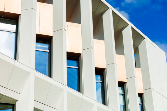 The building's façade is constructed of light-colored fiber cement panels with warm accents. Rectangular windows with black frames create a clean, contemporary style.
