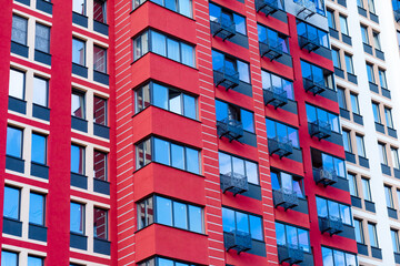 Fototapeta premium The multi-story building's façade is bright red with white vertical lines. Large windows and balconies with black metal railings create a modern and stylish look.