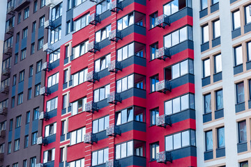The apartment building's façade features a contemporary style with vibrant red and gray stripes. The balconies are glazed, and the windows are large and glass, with black metal railings.