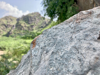 view of a textured granite stone, displaying natural patterns and mineral formations with a verdant mountain backdrop. Green mountains and rocky peaks under a cloudy summer sky