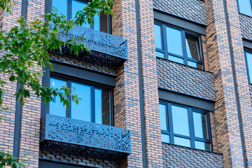 The building's brick façade features decorative metal balcony railings. Large windows with black frames create a modern and stylish look.