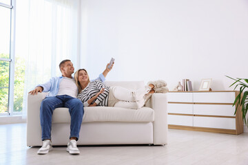 Obraz premium Woman and man using remote to control air conditioner on sofa at home