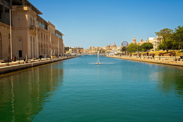  Urban landscape with a picturesque turquoise canal, historic buildings, metal bridge, and park with trees and benches.