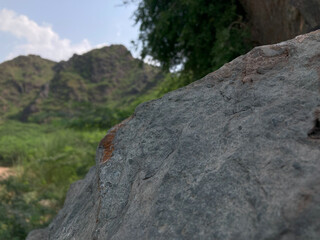 Ancient Rock and Verdant Valley,  close-up shot of a rough textured ancient rock sits in foreground, the blurred out background revealing verdant valley and rolling hills, showcasing natural beauty.