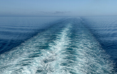 Tranquil view of the vast blue ocean with a boat’s wake stretching into the horizon under a clear blue sky.